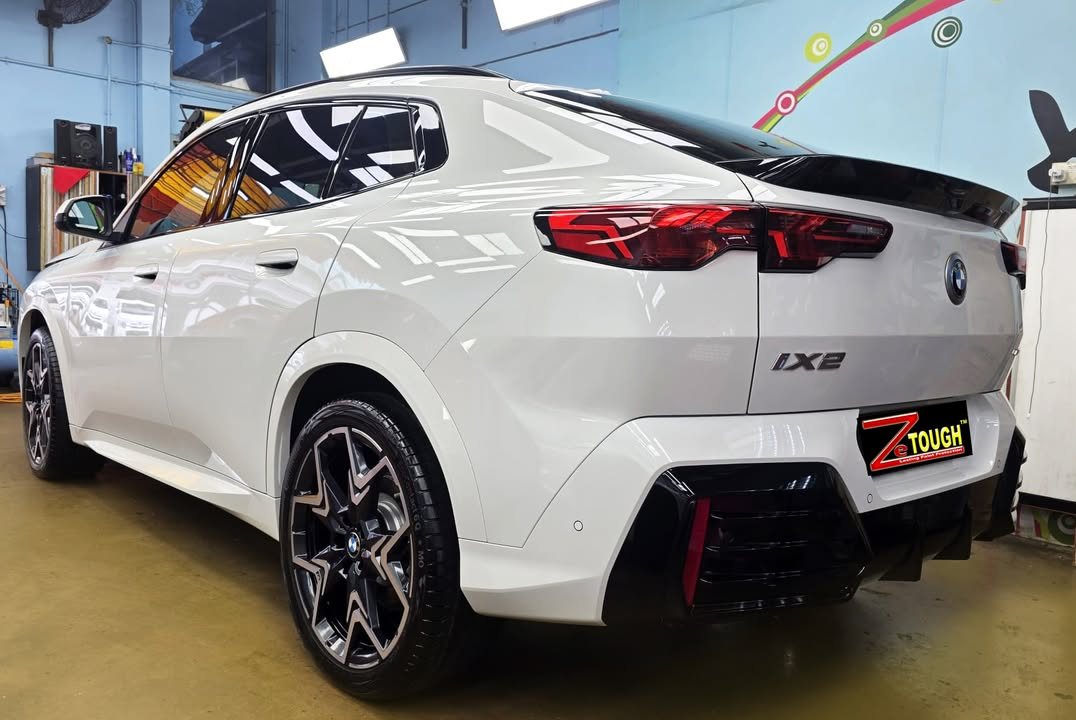 Rear three-quarter view of the white BMW iX2 with iX2 badge and ZeTough plate.