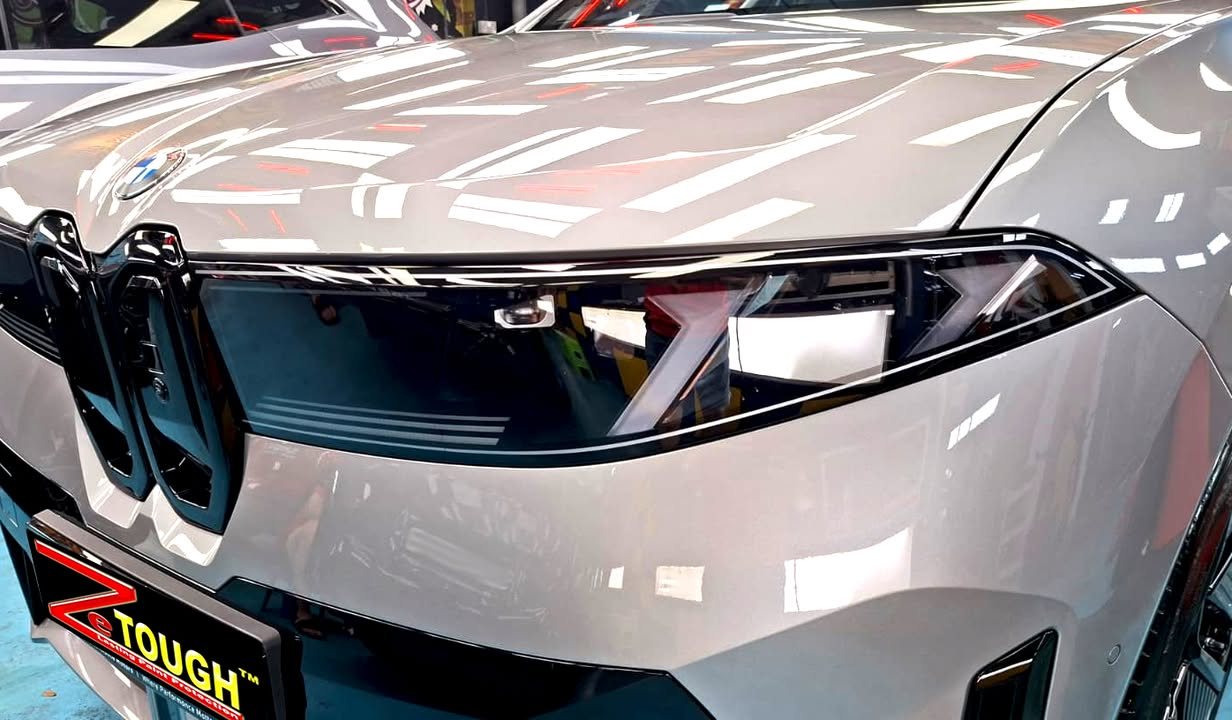Front of the grey iX3 showing the slim kidney grille and headlights, with light reflections across the bonnet.