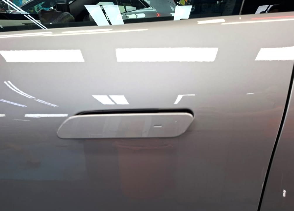 Flush door handle on the grey door panel with ceiling lights reflected in the paint.
