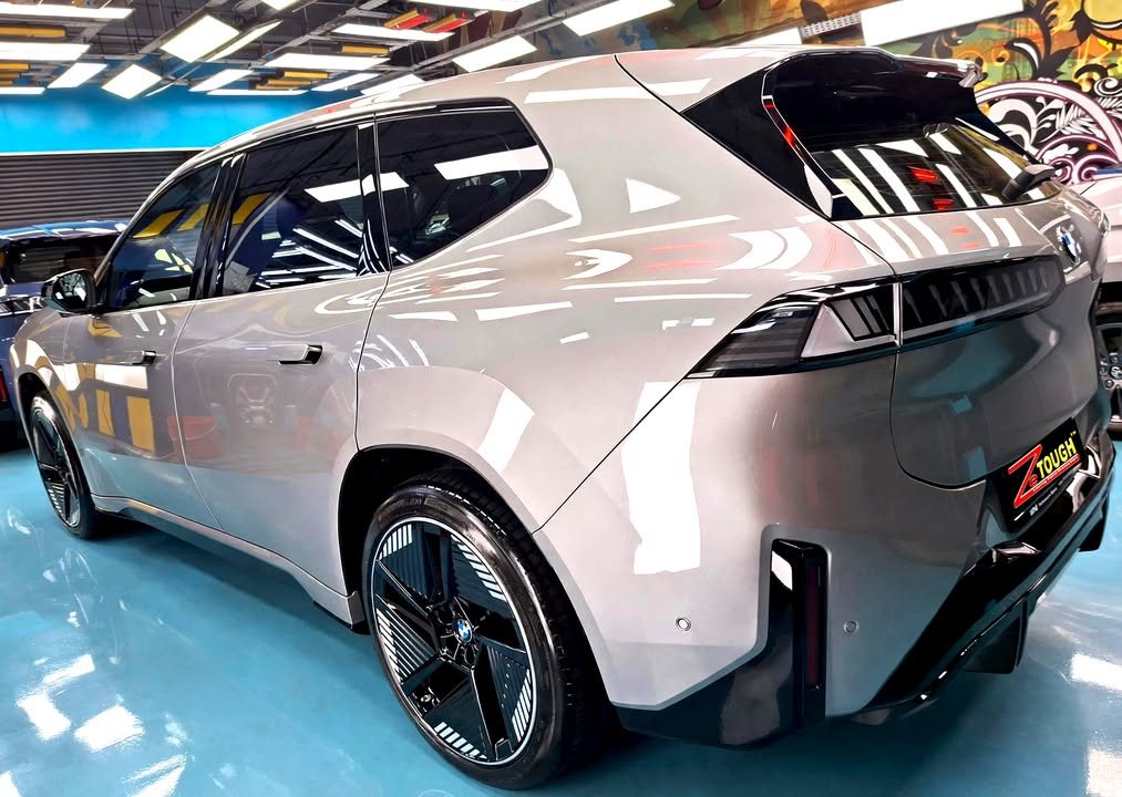 Rear three-quarter view of the grey BMW iX3 with black aero wheels.