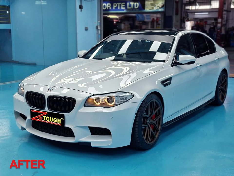 The finished white BMW M5 from the front three-quarter in the workshop, with dark wheels and red brake callipers.
