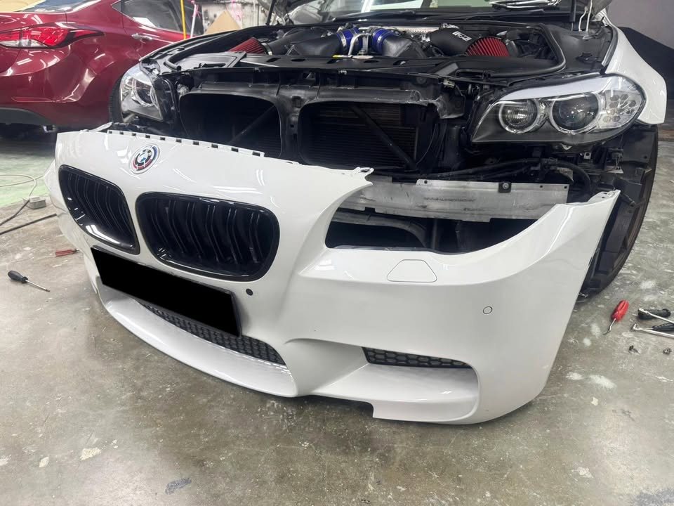 Front of the white M5 with the bumper off and headlamps exposed.