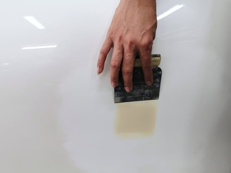 Hand sanding a yellow putty patch on the white panel.