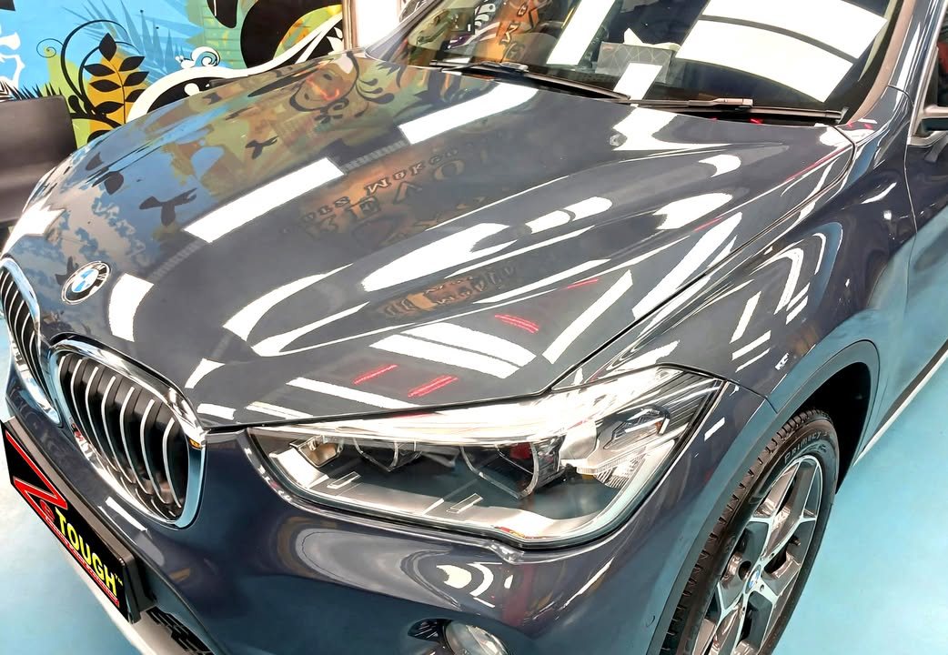 Bonnet, kidney grille and headlight of the blue BMW X1 reflecting the ceiling lights.