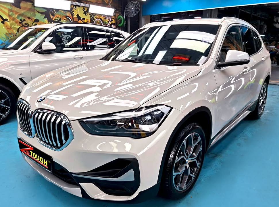 White BMW X1 from the front three-quarter on the workshop's blue floor.