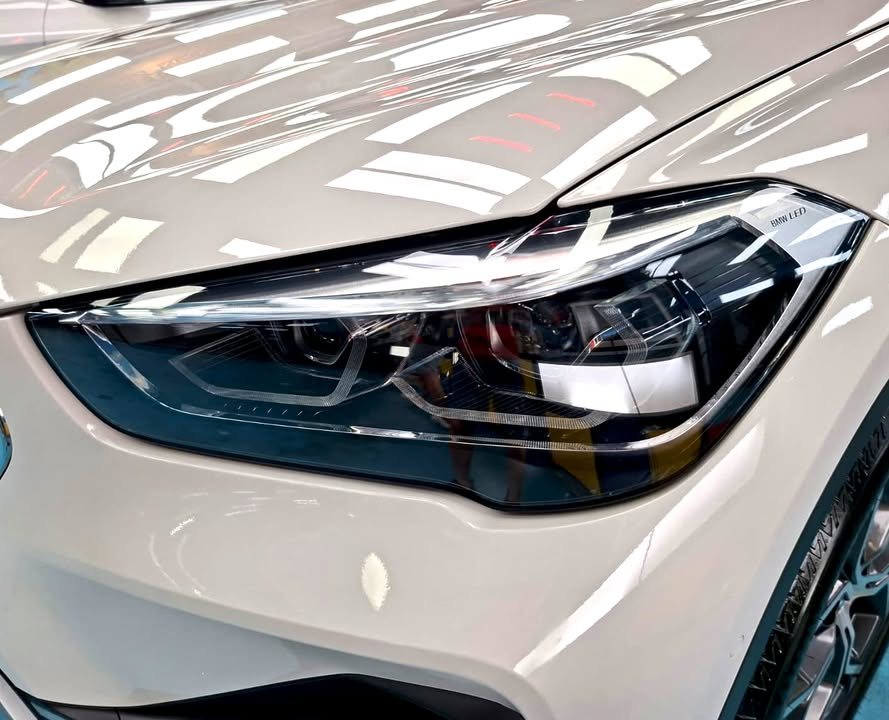 Close-up of the X1 headlight and white bonnet edge with sharp reflections.