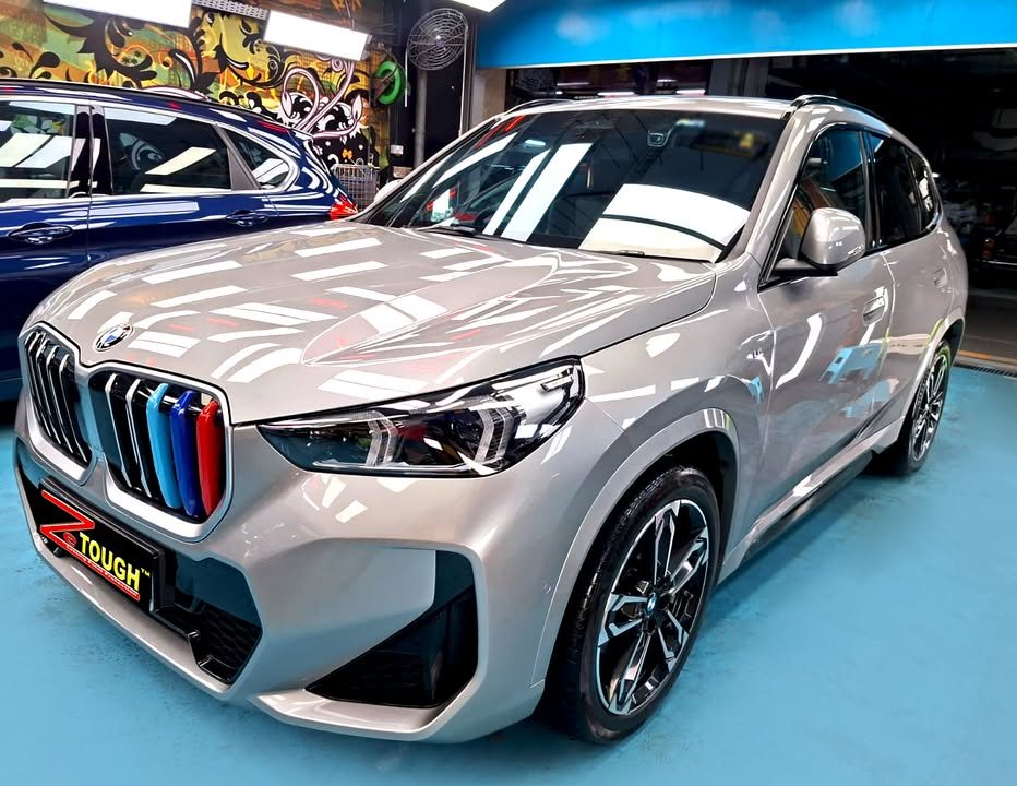Front three-quarter view of the grey BMW X1 in the workshop, with M-striped kidney grille and two-tone wheels.