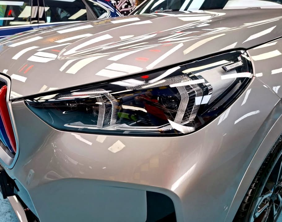 Close-up of the headlamp with light reflections on the grey bonnet and wing.