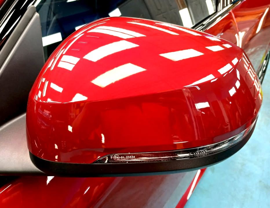 Red side mirror cap on the X2 reflecting the ceiling lights.