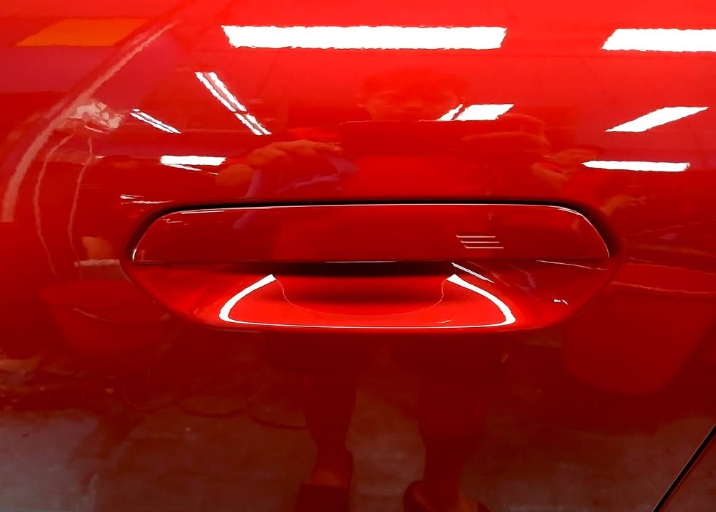 Red door panel and handle with a mirror-like reflection.
