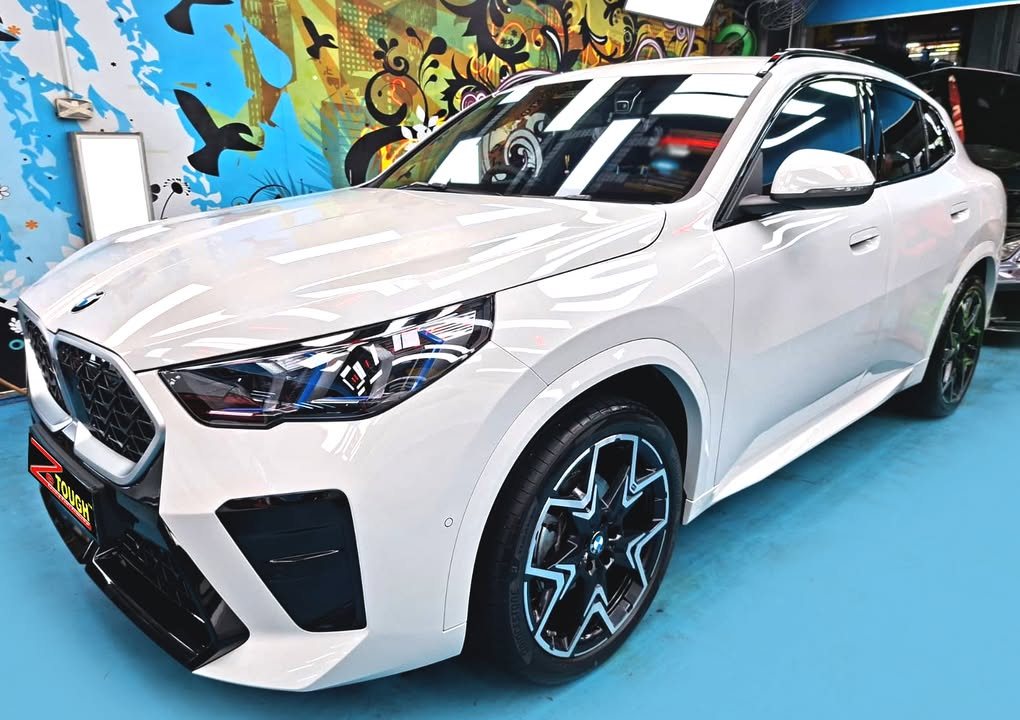 White BMW X2 from the front three-quarter in the Revol workshop, with a ZeTough plate on the bumper.