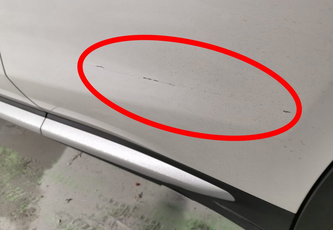 The BMW X3 from the side on arrival, surface marks visible across the panels.