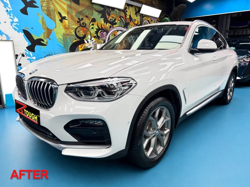 The finished white BMW X4 from the front three-quarter in the workshop, paint glossy under the lights.