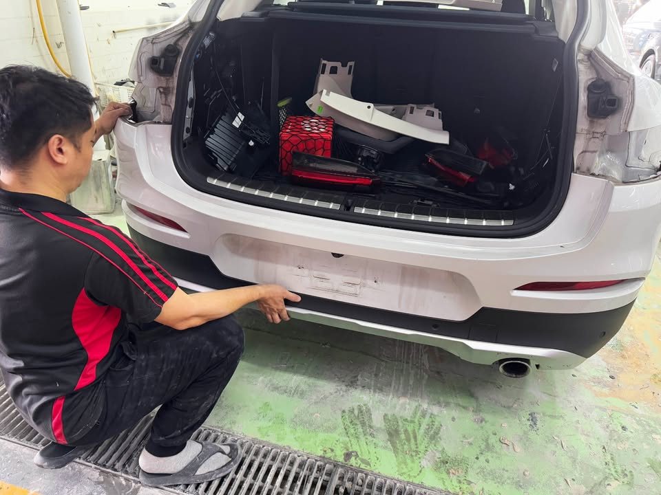 Technician removing the rear bumper parts of the X4 with the tailgate open.