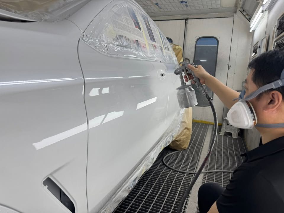 Painter in a respirator spraying the side of the white X4 in the spray booth.