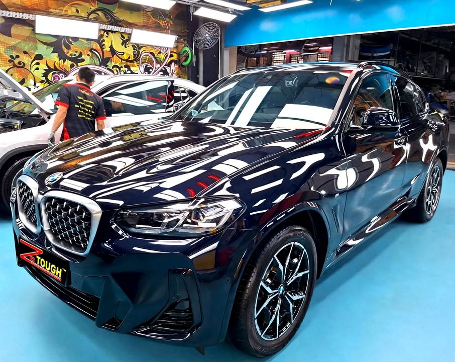 Front three-quarter view of a dark blue BMW X4 in the Revol Carz hall, lights reflected across the bonnet.