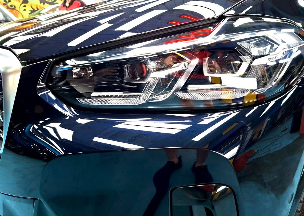 Close-up of the X4 headlight and front wing in dark blue paint.