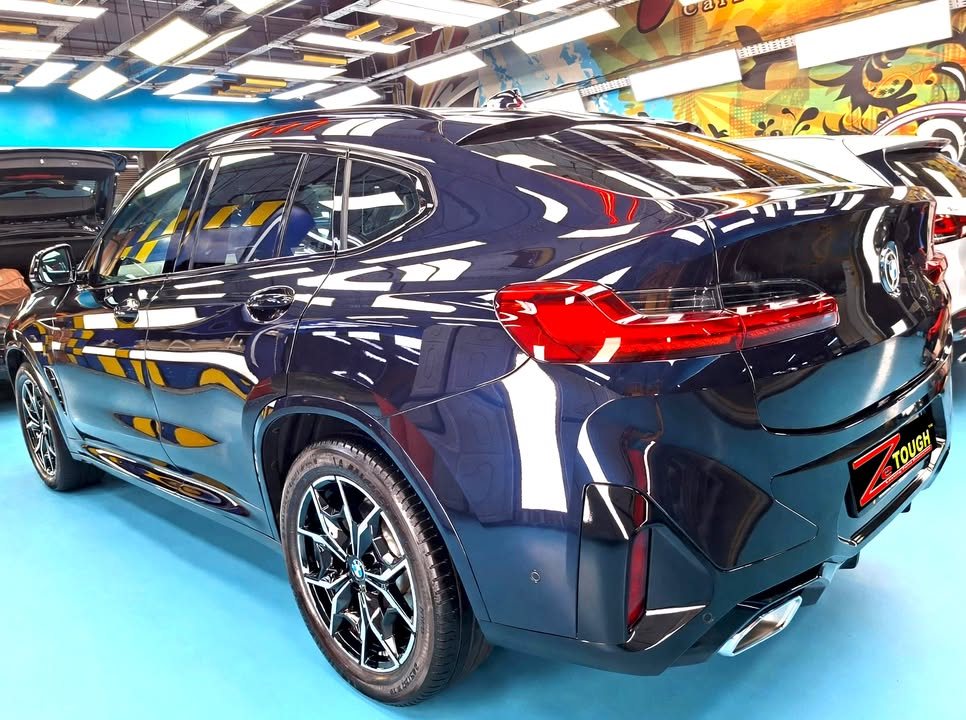 Rear three-quarter view of the dark blue BMW X4 showing the tail lights.