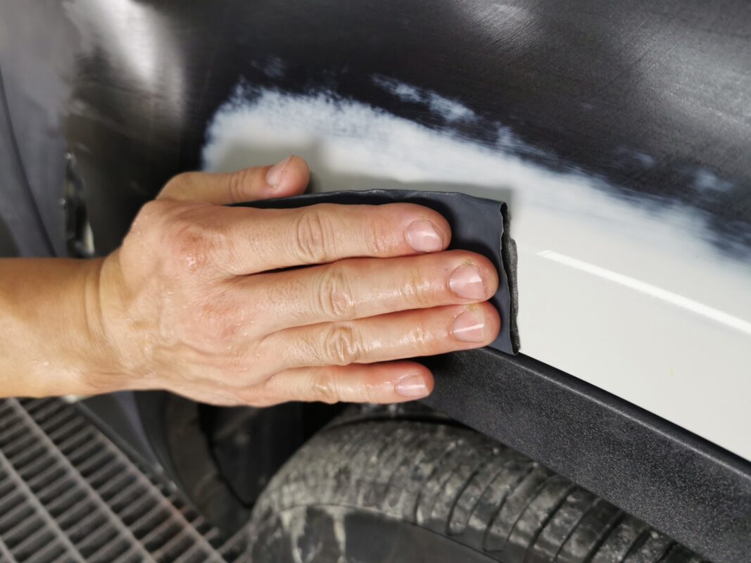 Wet-sanding a panel on the BMW X6 to achieve a smooth, level surface.