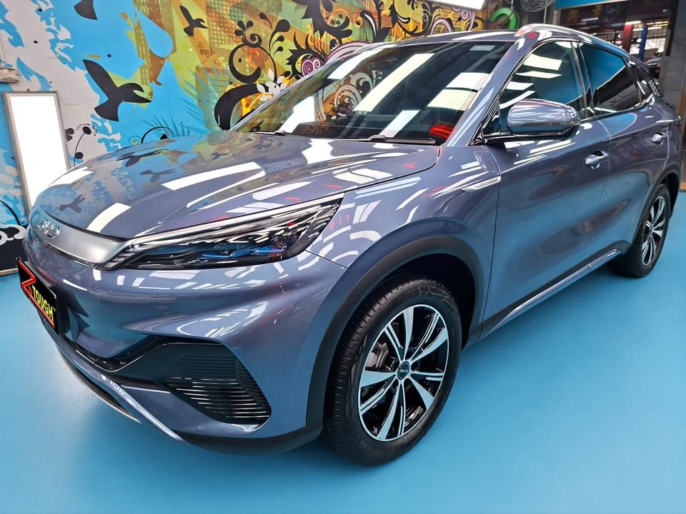 Blue-grey BYD Atto 3, front three-quarter view in the workshop with a ZeTough plate on the bumper.