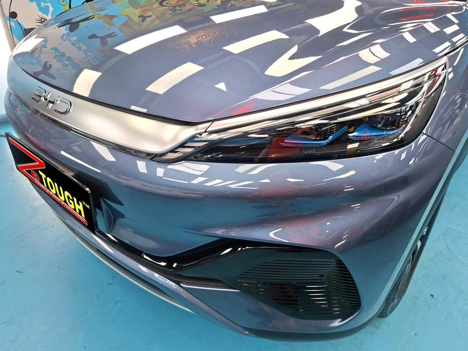 Front of the blue-grey BYD Atto 3 showing the headlamp and bonnet reflections.