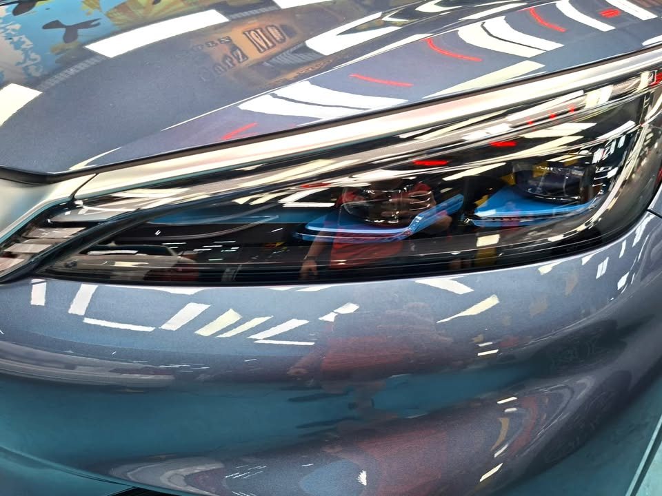 Close-up of the BYD Atto 3 headlamp with workshop lights reflected in the paint.