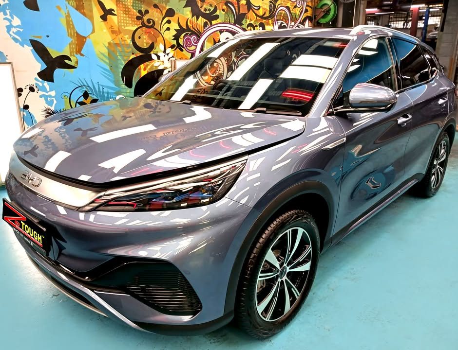 Grey-blue BYD Atto 3, front three-quarter view, with workshop lights reflected on the bonnet after its ZeTough Titanium coating.