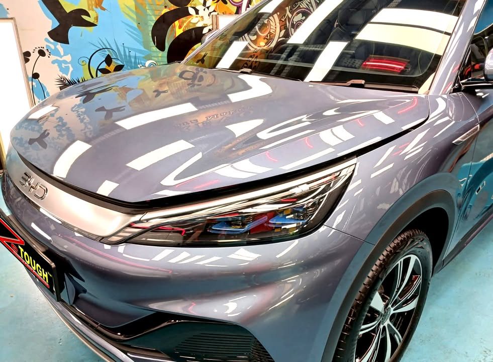 Grey-blue bonnet and front of the Atto 3 reflecting the ceiling lights.
