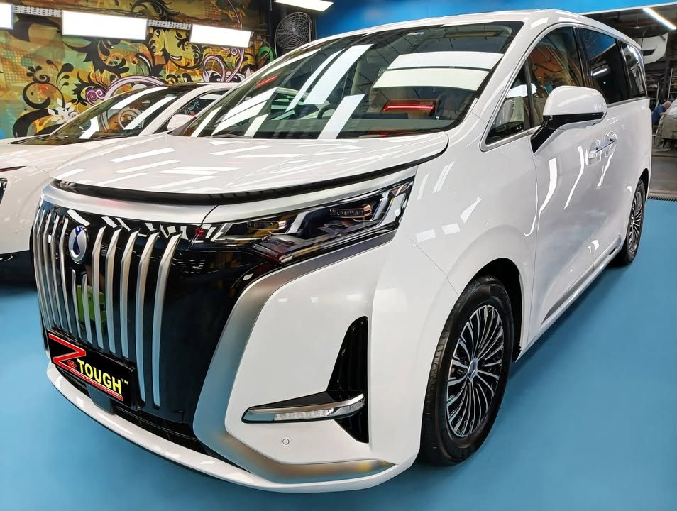 White BYD Denza D9 MPV, front three-quarter view in the workshop showing the vertical-bar grille.