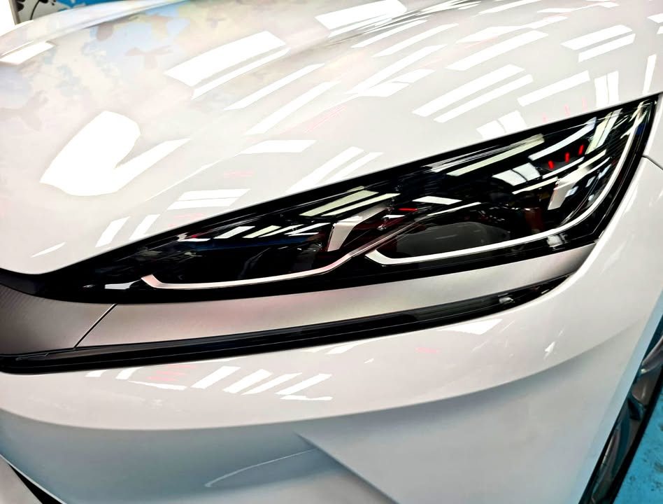 Close-up of the slim headlight and white bonnet edge with sharp reflections.