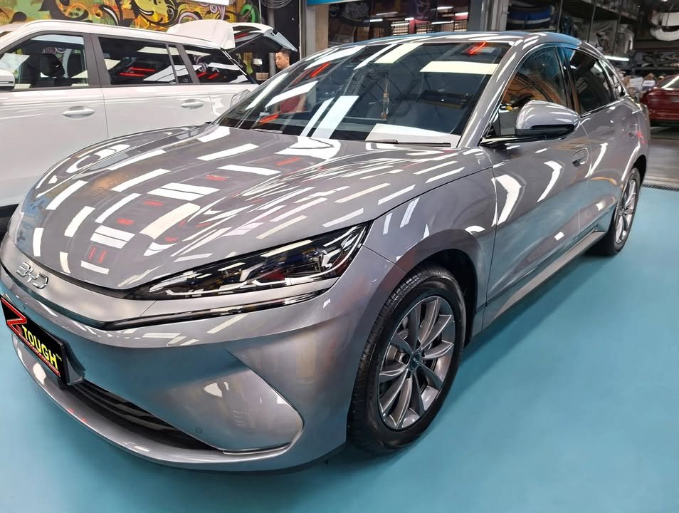 Front three-quarter view of the grey BYD Seal 6 in the workshop, ceiling lights reflected across the bonnet.