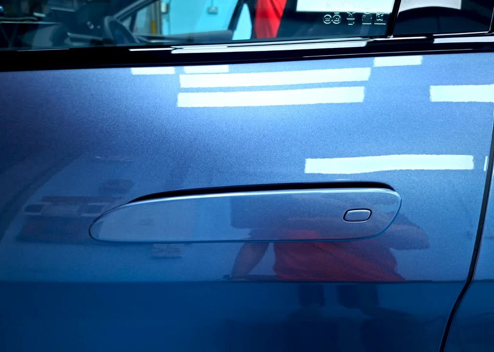 Door panel with a flush handle and light reflections in the blue grey paint.