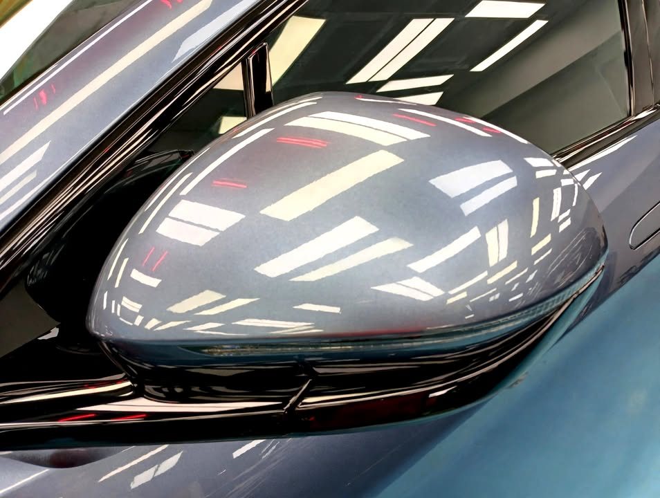 The blue-grey wing mirror reflecting the workshop ceiling lights.