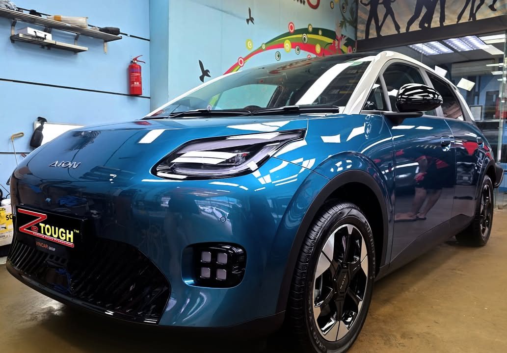 Blue GAC AION with a white roof, front three-quarter view in the workshop with a ZeTough plate.
