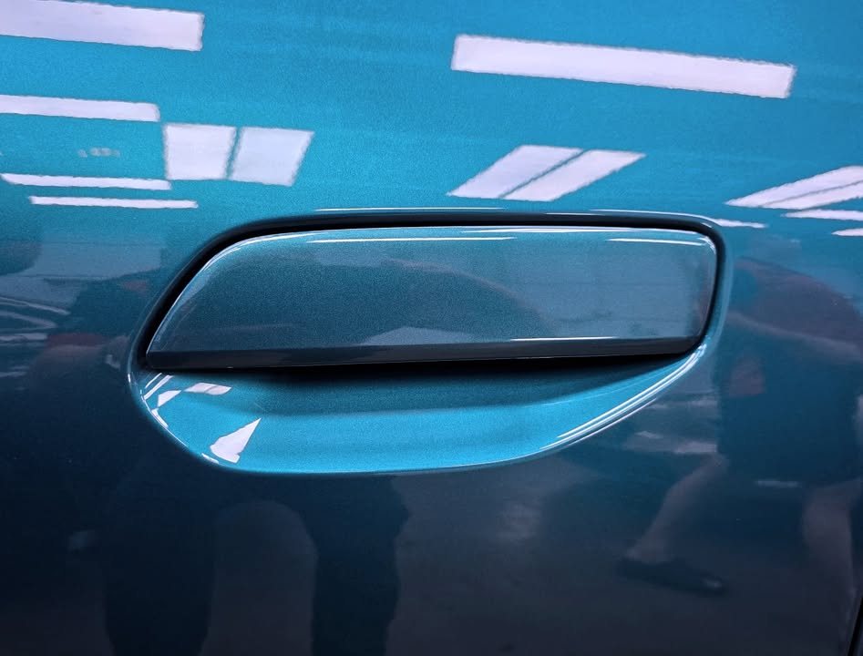 Flush door handle on the blue GAC AION with workshop lights reflected in the paint.