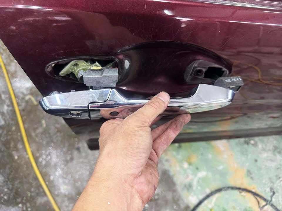 Hand removing the chrome door handle from the maroon door.