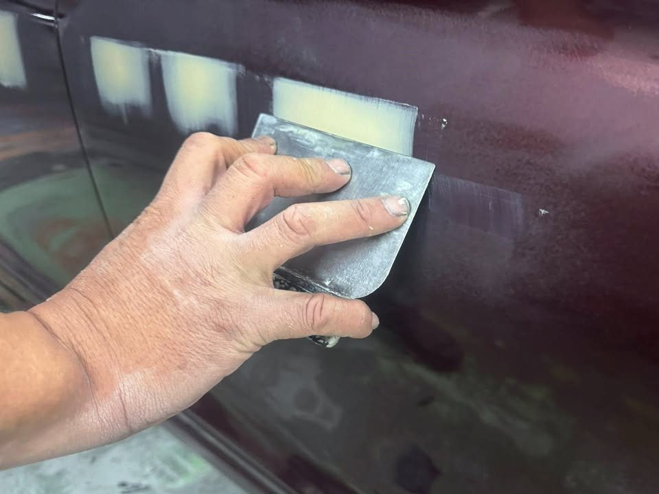 Hand spreading filler over a door panel with a spreader.