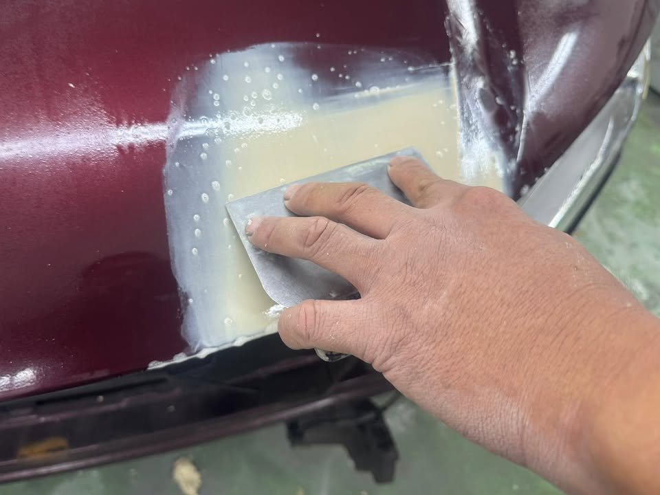 Wet-sanding a primed patch on the front of the Honda City.