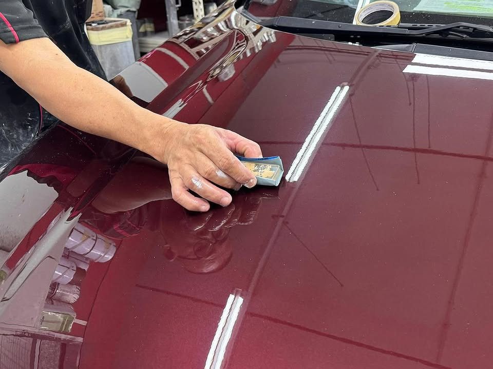 Hand wet-sanding the maroon bonnet of the Honda City.