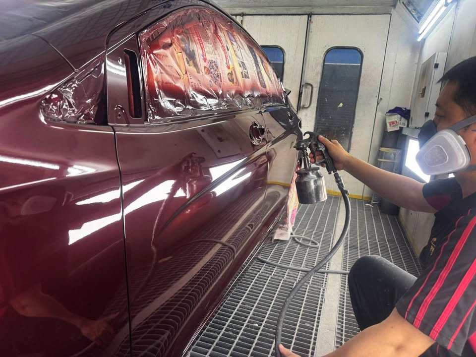 Painter in a mask spraying the maroon side of the Honda City in the spray booth.