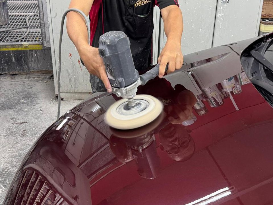 Team member machine polishing the newly painted maroon bonnet.