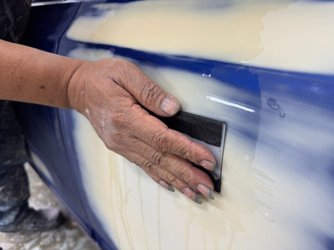 Wet-sanding the body of the Honda Civic to smooth the surface.