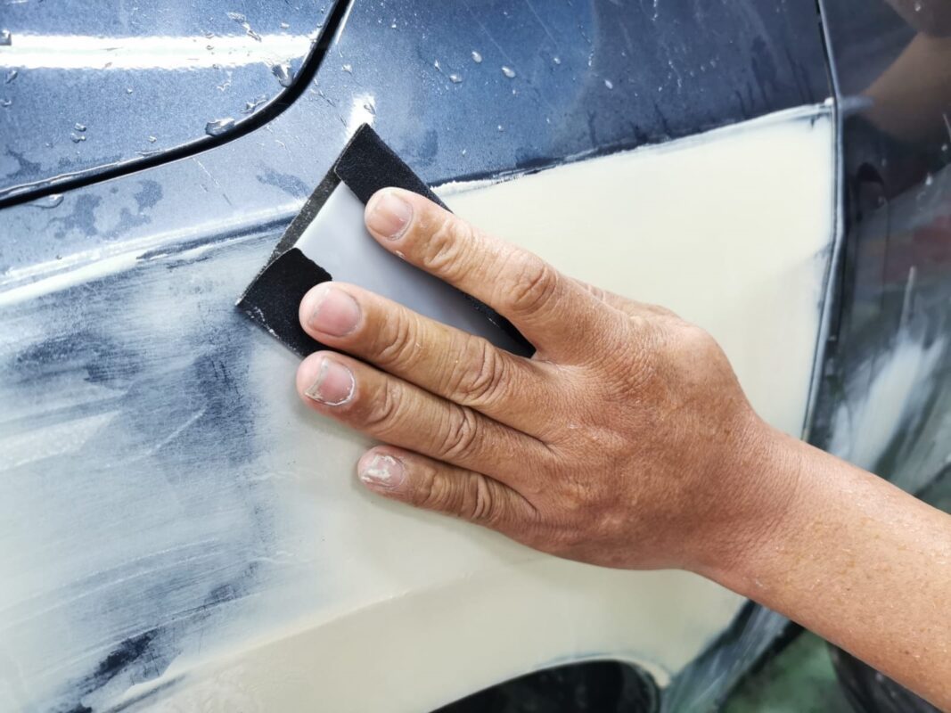 Wet-sanding a panel of the Honda Civic to level the surface.