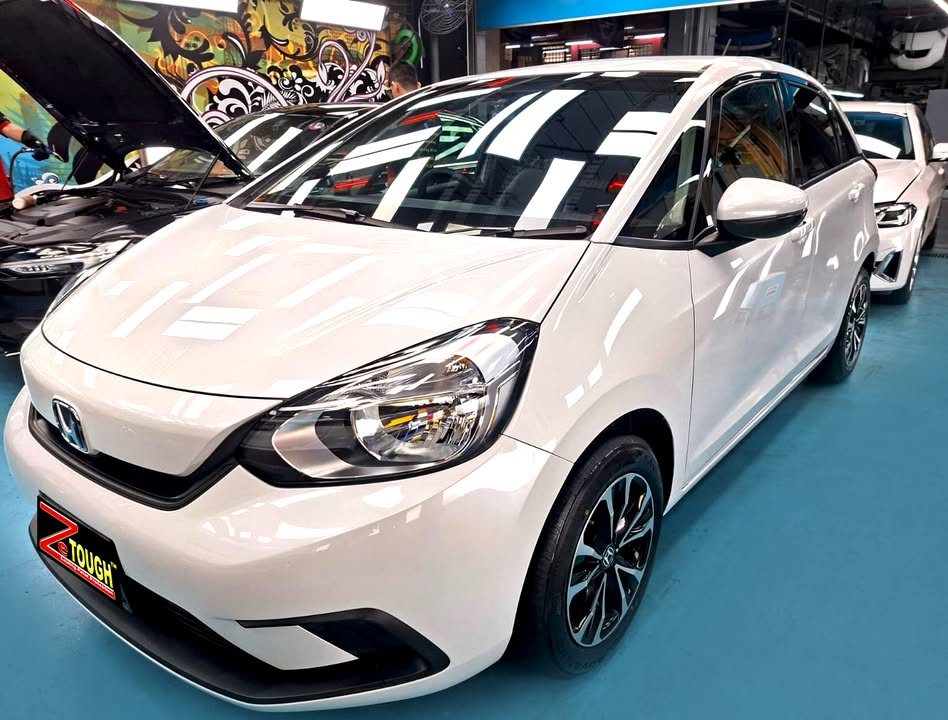 White Honda Fit hatchback, front three-quarter view, in the Revol Carz workshop after coating.