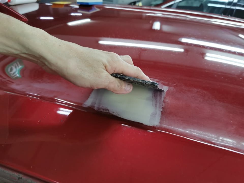 Spreading putty over a scratch on the red HR-V's panel.