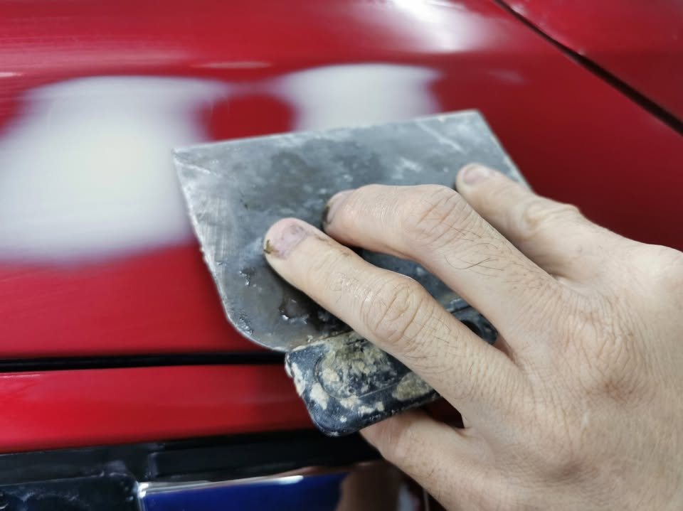 Putty knife smoothing filler on the HR-V's lower door.