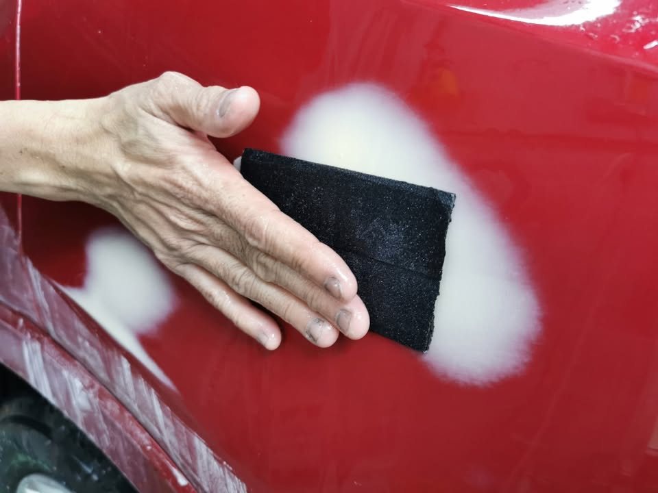 Sanding pad levelling white putty patches on the red bodywork.