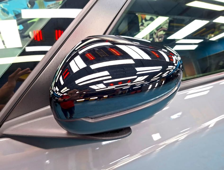 Gloss black side mirror cap reflecting the workshop ceiling.