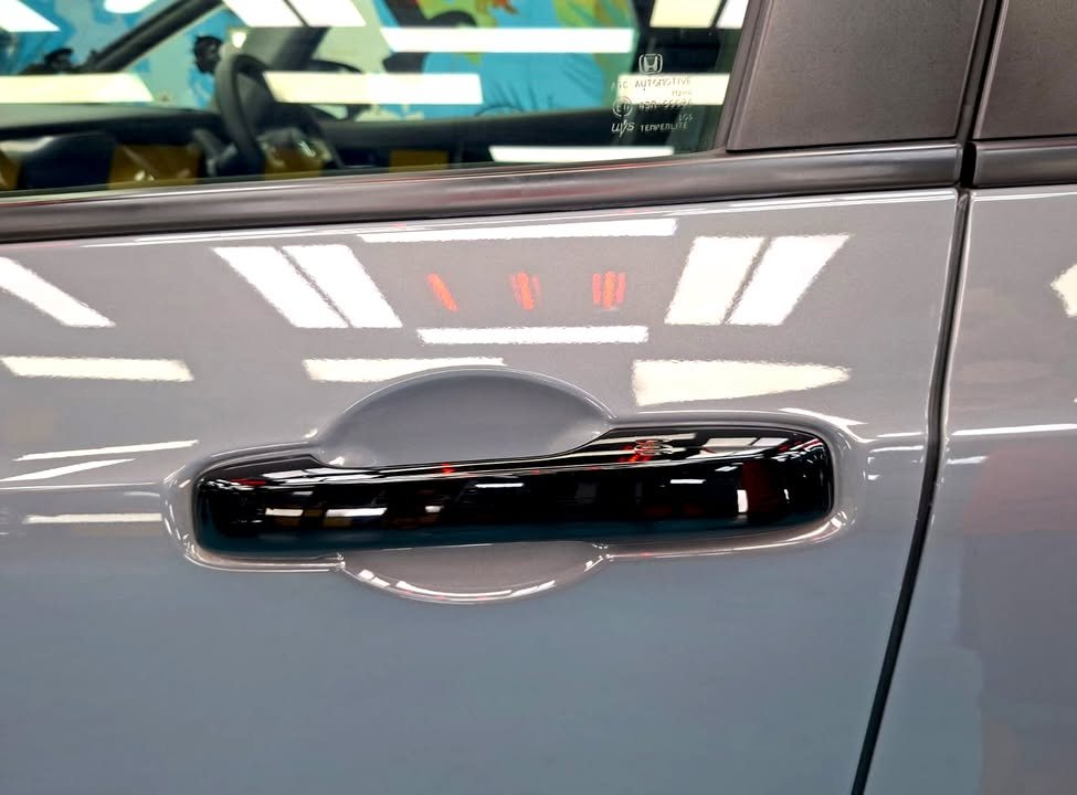Grey door panel with a gloss black handle and sharp light reflections.