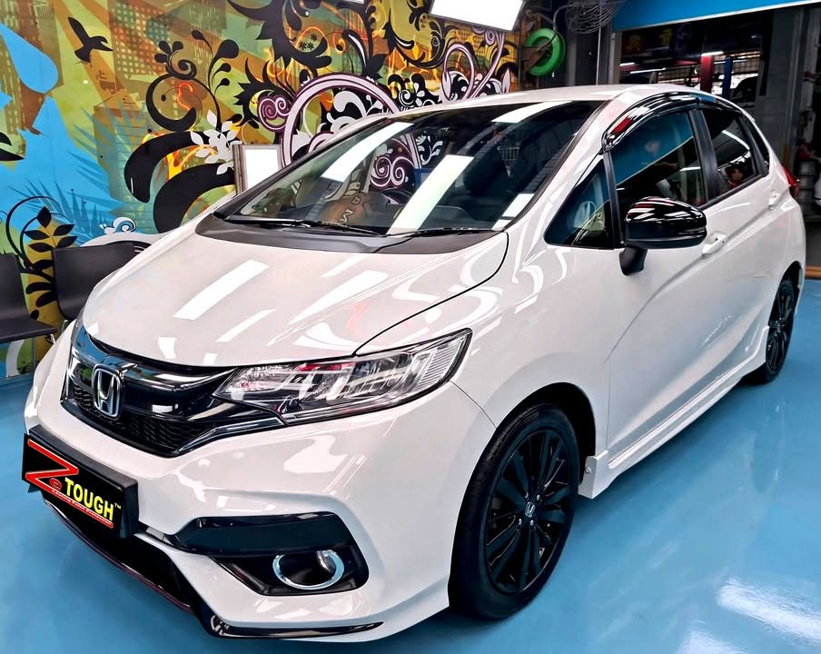Front three-quarter view of the white Honda Jazz with black wheels in the workshop.